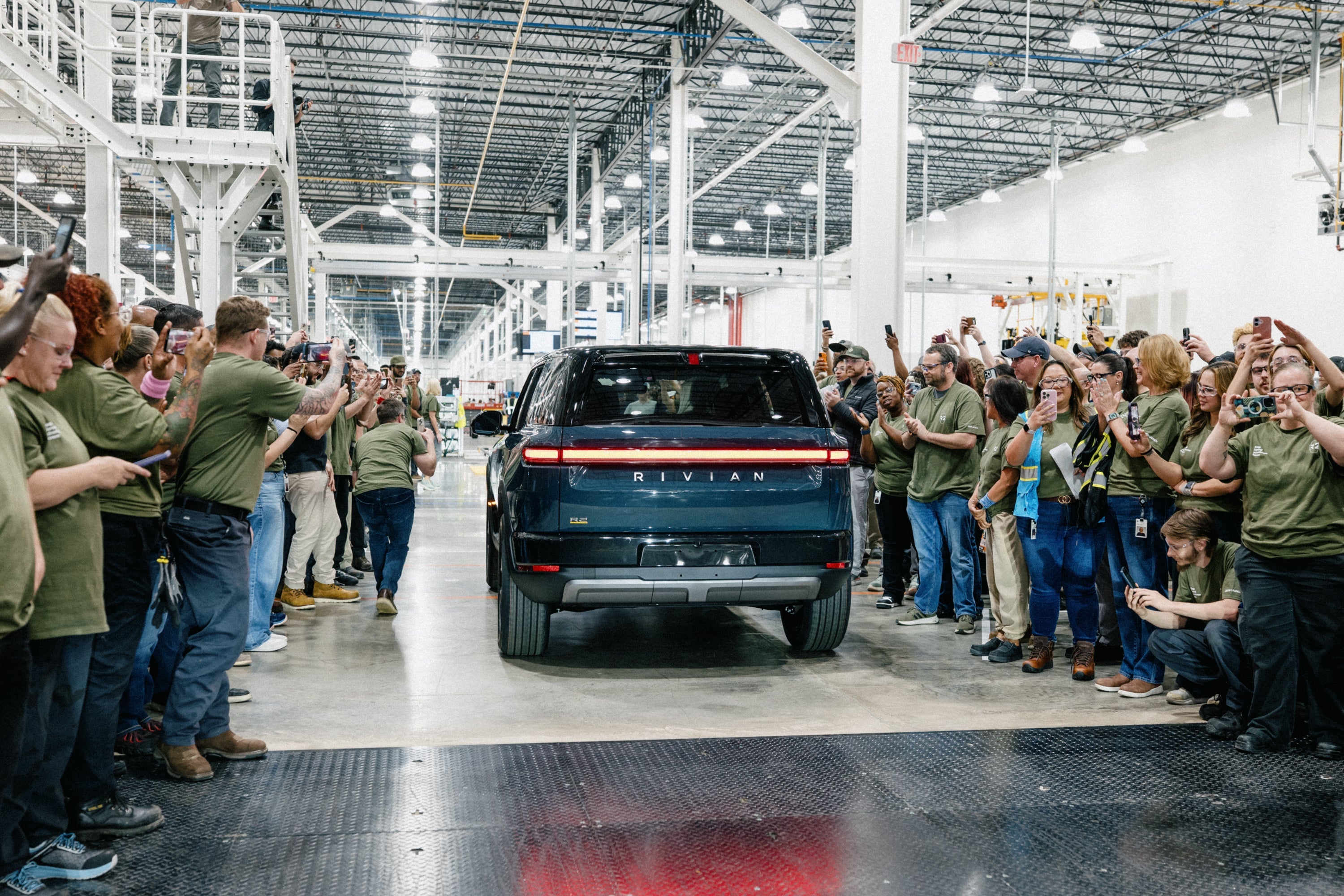 Group of people in green shirts gathered around a black SUV in a factory setting.