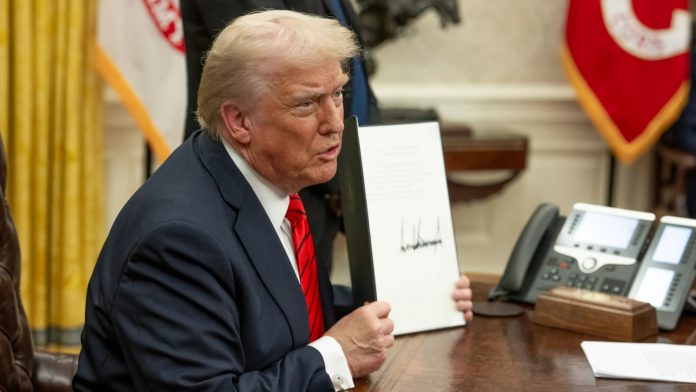 President Trump signing a document at a desk with flags.