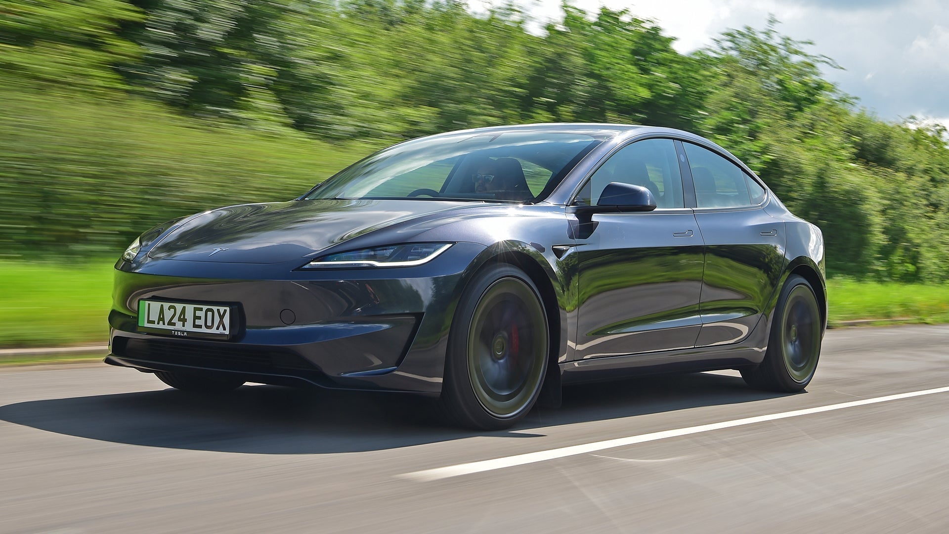 Black Tesla car speeding on a road with green surroundings.