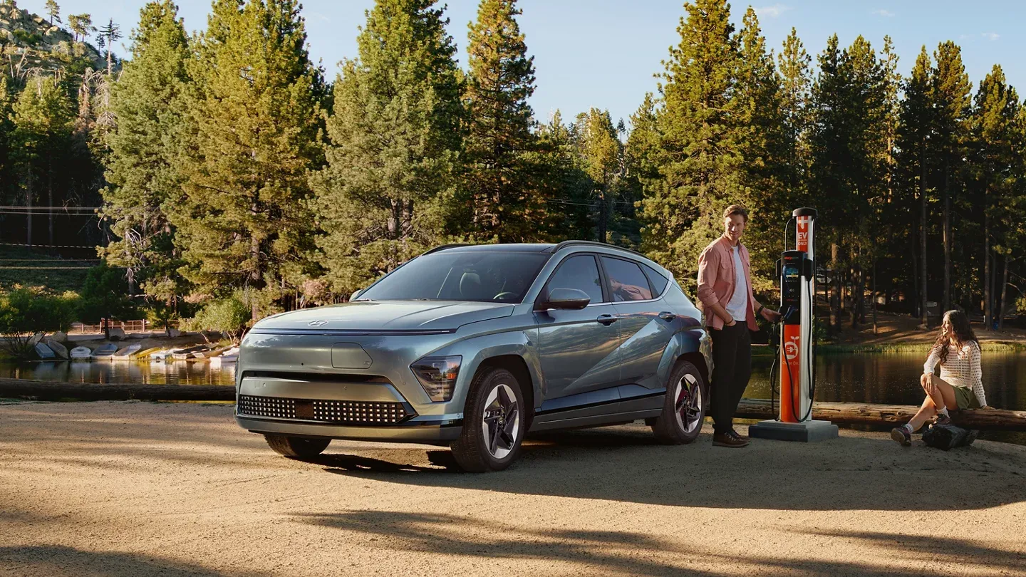 Couple with grey EV at charging station by lake.