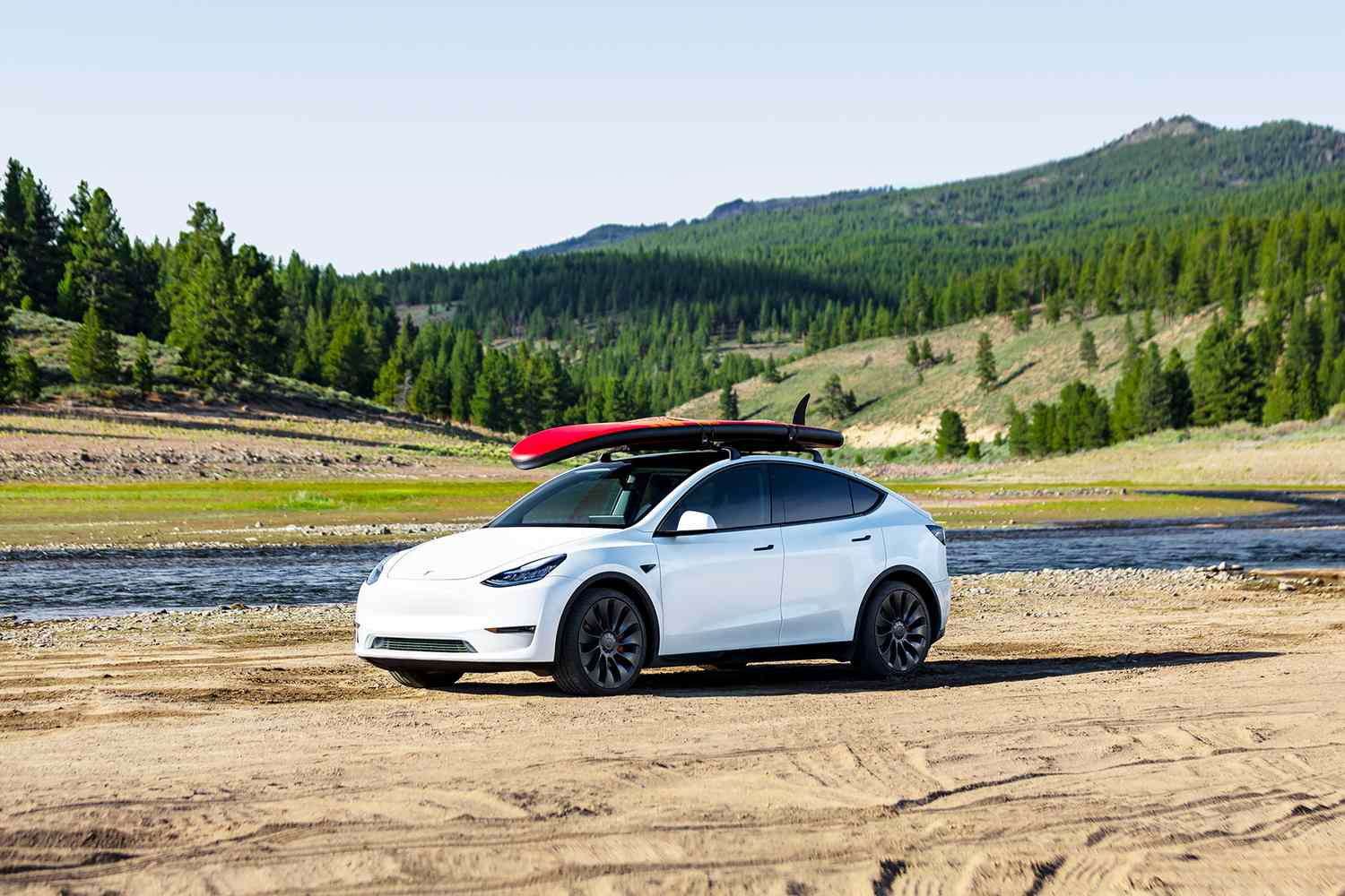 White Tesla EV with kayak by river and forest.