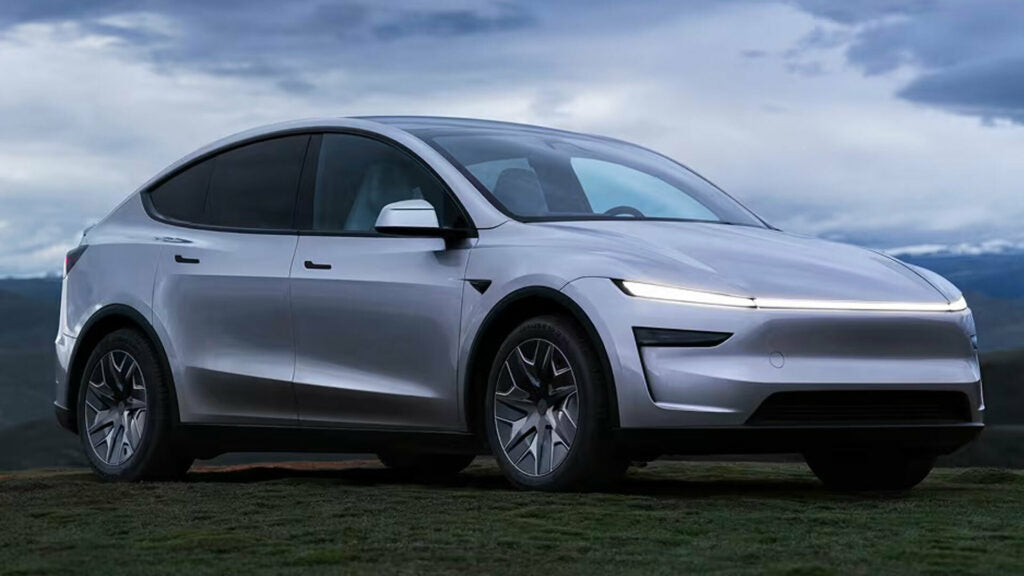 Tesla Model YL parked at grass, cloudy sky and mountains at the background.