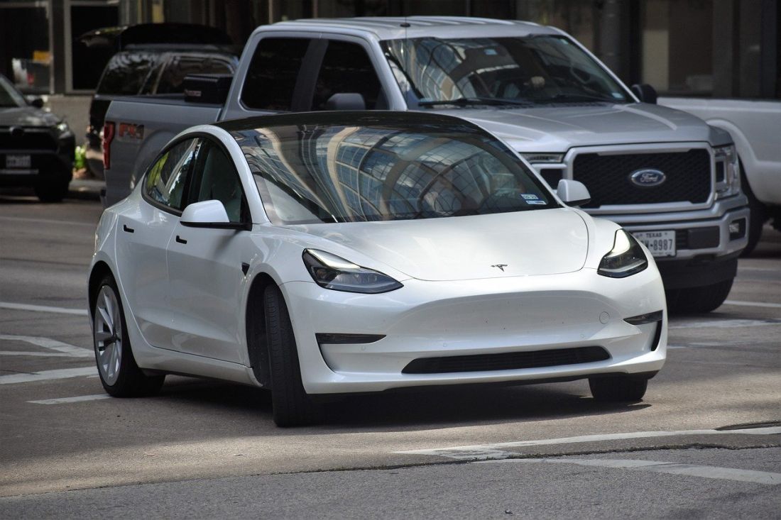 White Tesla Model 3 car driving on a city street with other vehicles.