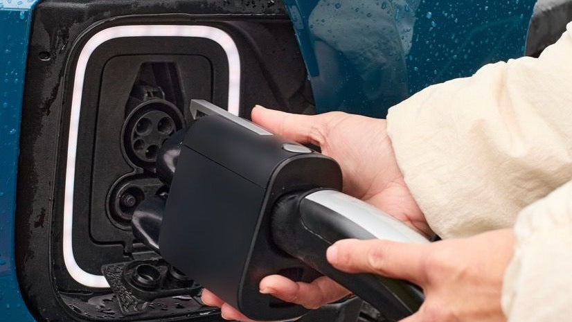 Person plugging Tesla Supercharger into a blue EV's charging port.